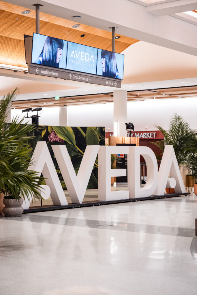 Large Aveda branding at a professional industry event highlighting the community and networking benefits of a salon brand partnership.